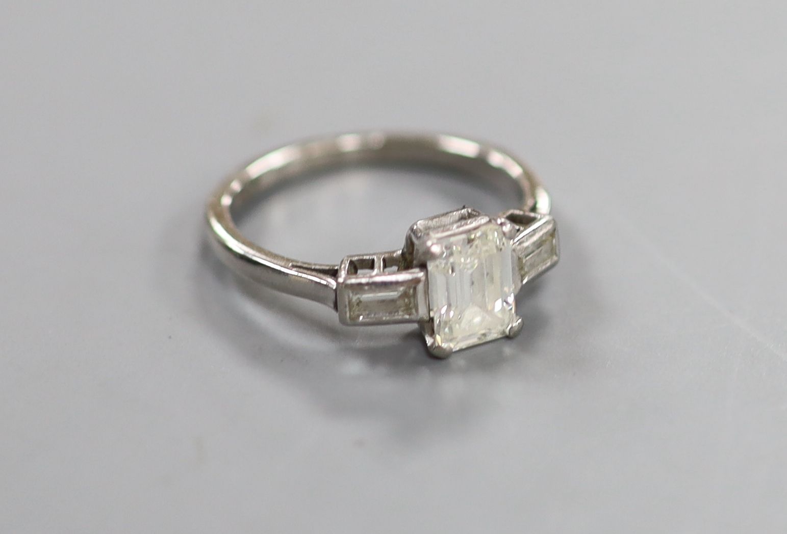 A white metal and emerald cut single stone diamond ring, with baguette cut diamond set shoulders